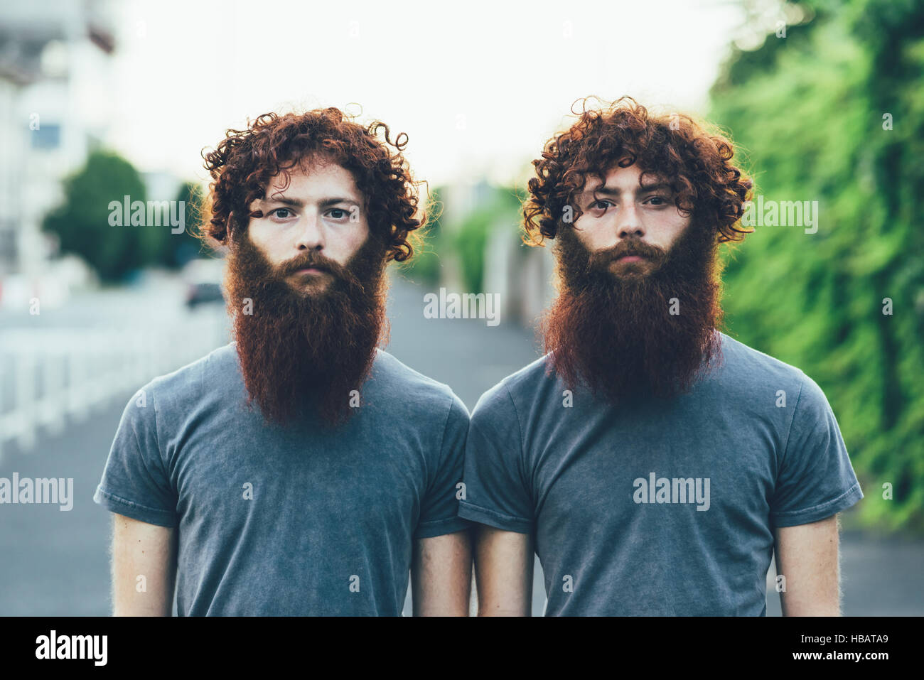 Portrait of identical adult male twins with red hair and beards on sidewalk Stock Photo