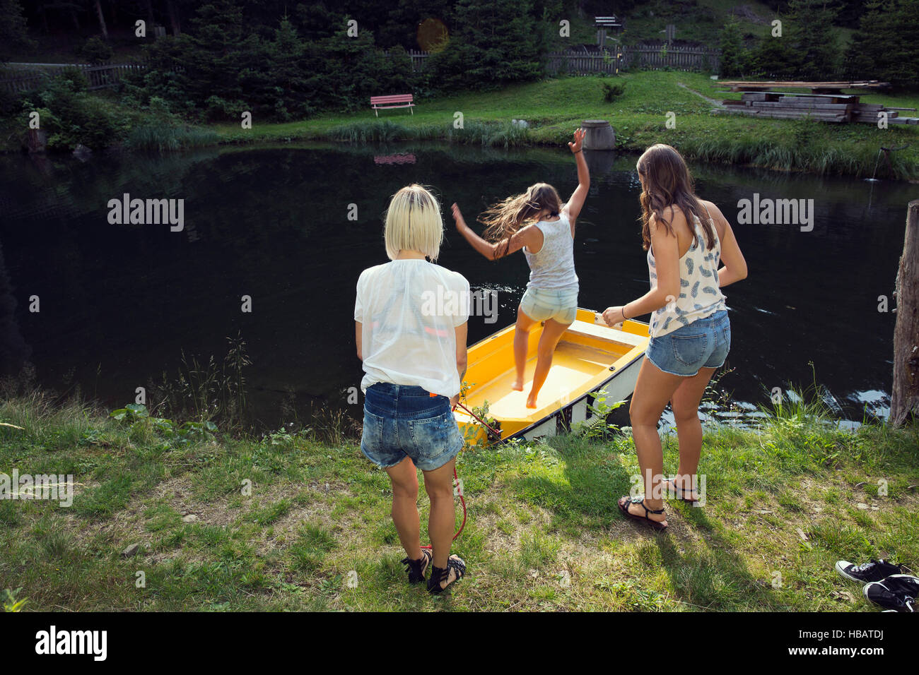 Three adult female friends jumping into rowing boat on lake, Sattelbergalm, Tirol, Austria Stock Photo