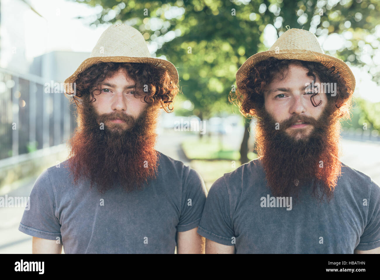Portrait of identical male hipster twins wearing straw hats on sidewalk Stock Photo