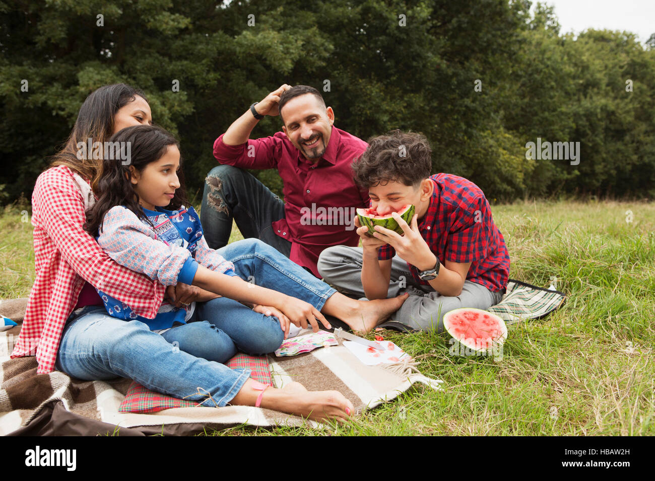 Family sitting outdoors, on picnic blanket, son eating watermelon Stock