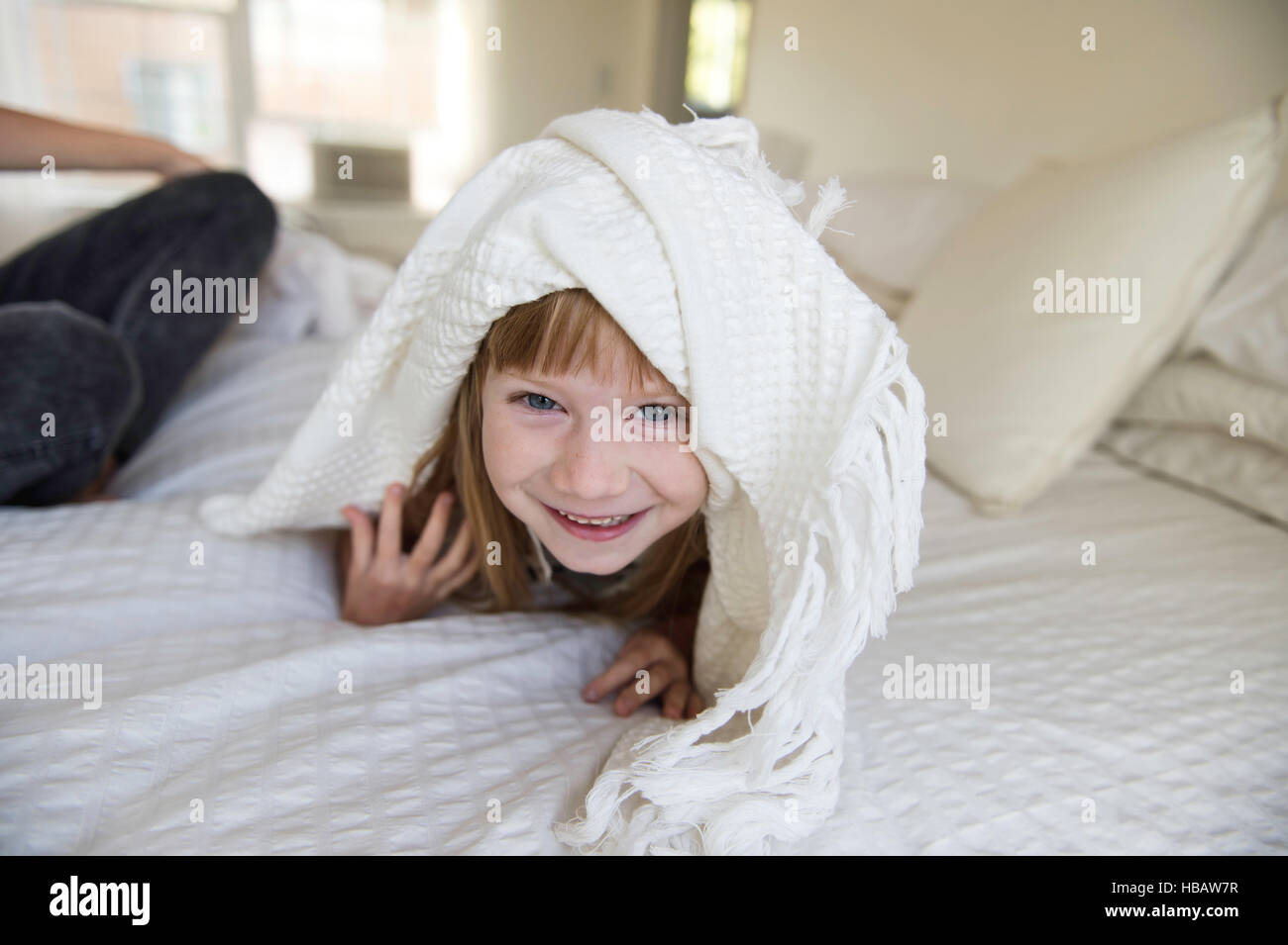 Young girl peeking head out from under blanket on bed Stock Photo