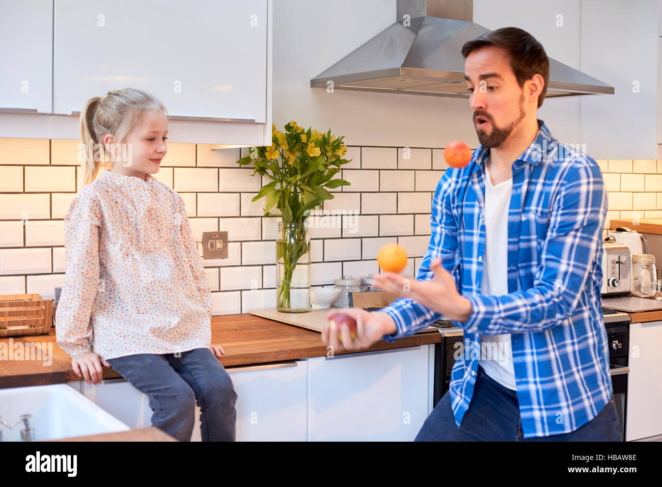 Mid adult man juggling fruit for daughter in kitchen Stock Photo