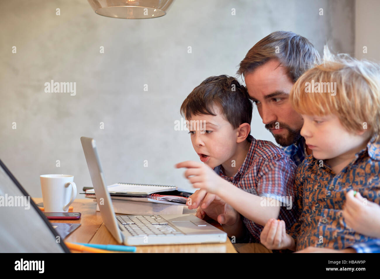Mid adult man looking at laptop with two sons at dining table Stock Photo