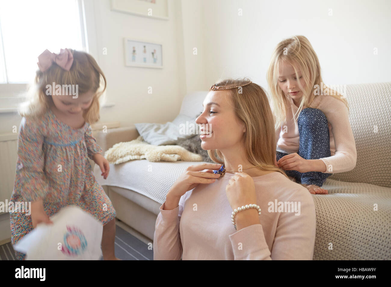 Girl putting necklace onto mother in living room Stock Photo