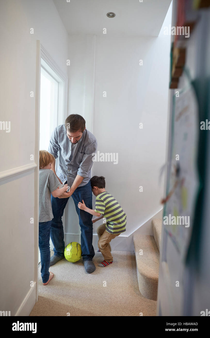 Mid adult man playing soccer with sons in hallway Stock Photo
