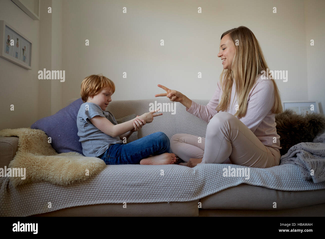 Mid adult woman and son playing rock-paper-scissors on sofa Stock Photo