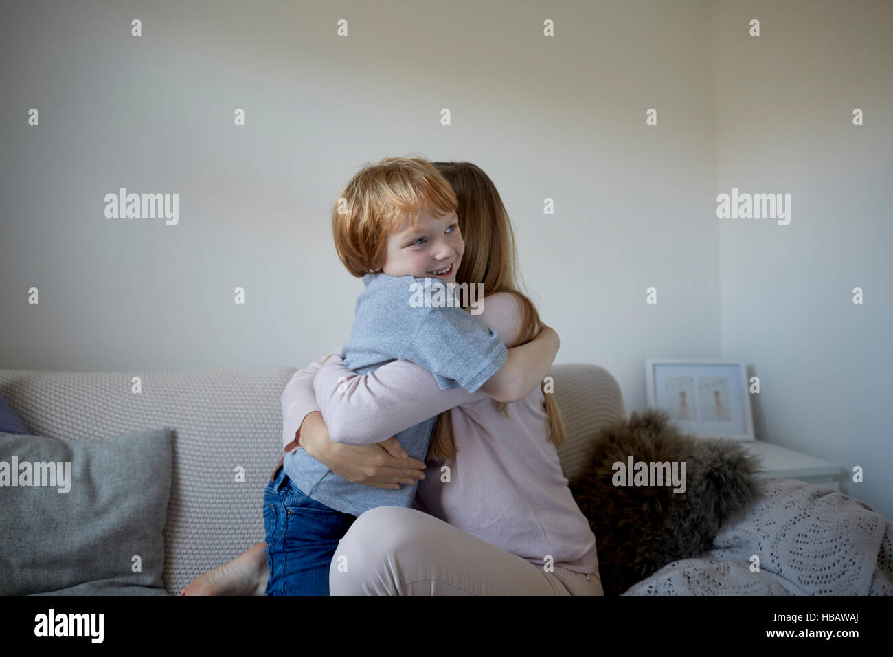 Mid adult woman and son hugging on sofa Stock Photo