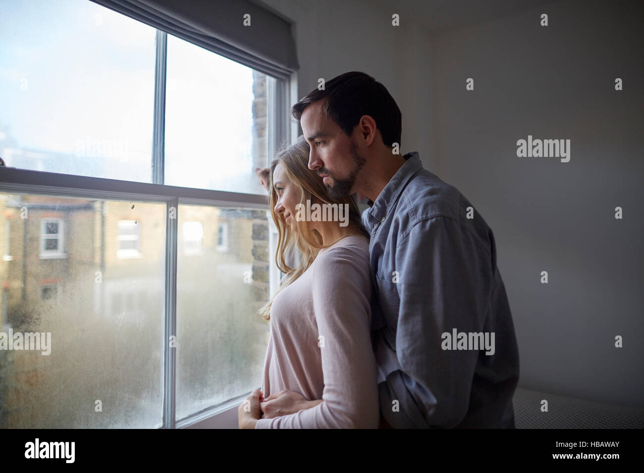 Mid adult couple gazing out through bedroom window Stock Photo