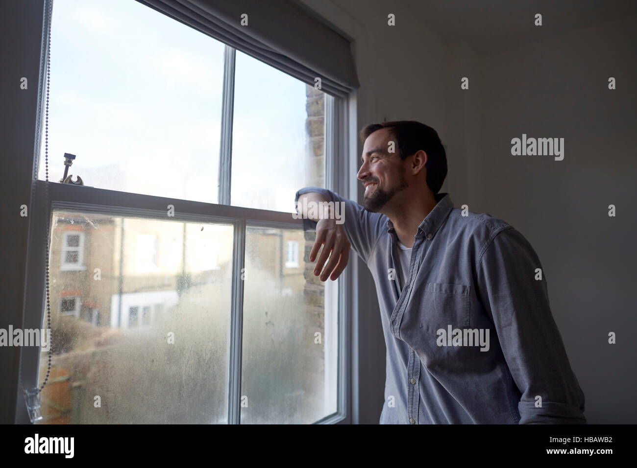 Mid adult man looking out through bedroom window Stock Photo