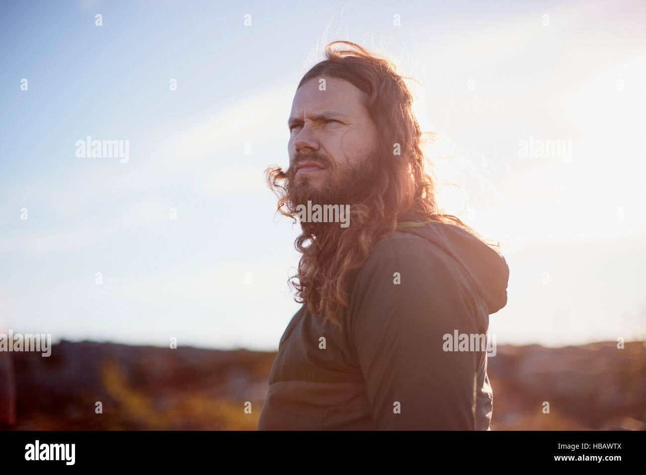 Man with long hair frowning in hot sun Stock Photo