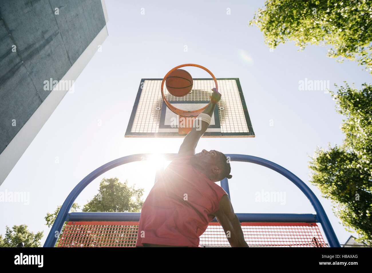 Young male basketball player throwing ball in sunlit basketball hoop Stock Photo