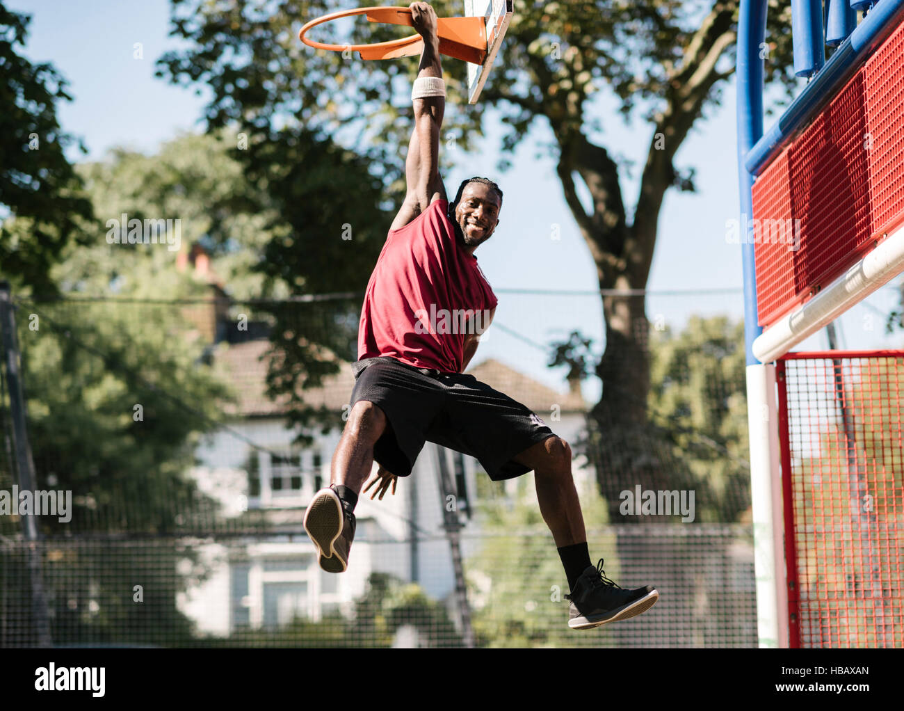 Portrait of young male basketball player hanging from basketball hoop Stock Photo