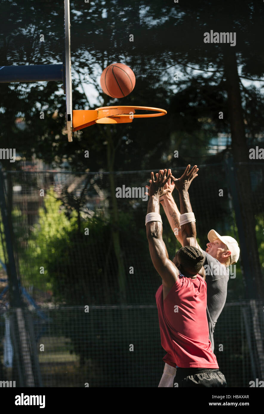 Young male basketball players throwing ball at basketball hoop Stock Photo