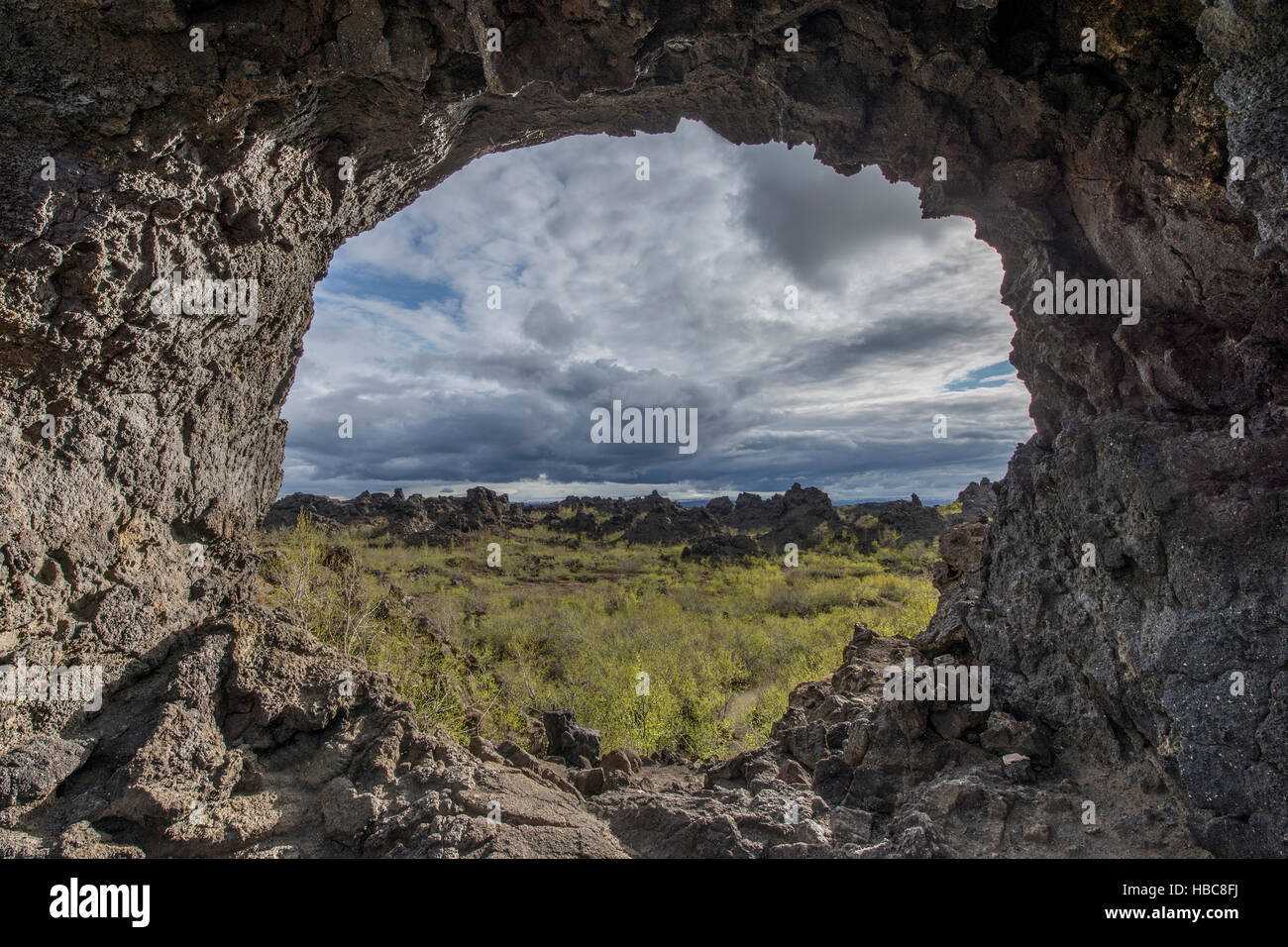 A round natural window in the volcanic rocks overlooking lava field covered by the vegetation. Stock Photo