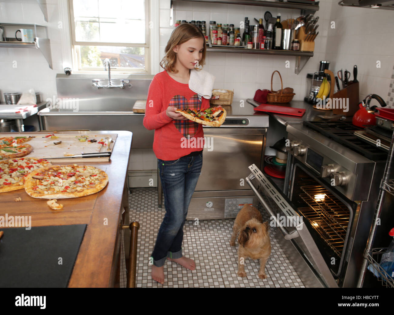 Young girl in kitchen, putting pizza in oven Stock Photo