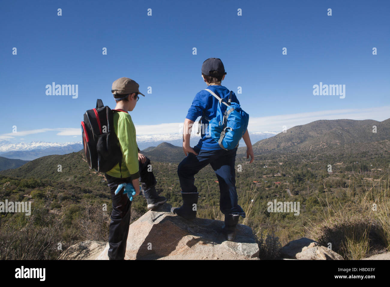 Rear view of two boys standing on boulder looking out over Andes, Valparaiso, Chile Stock Photo