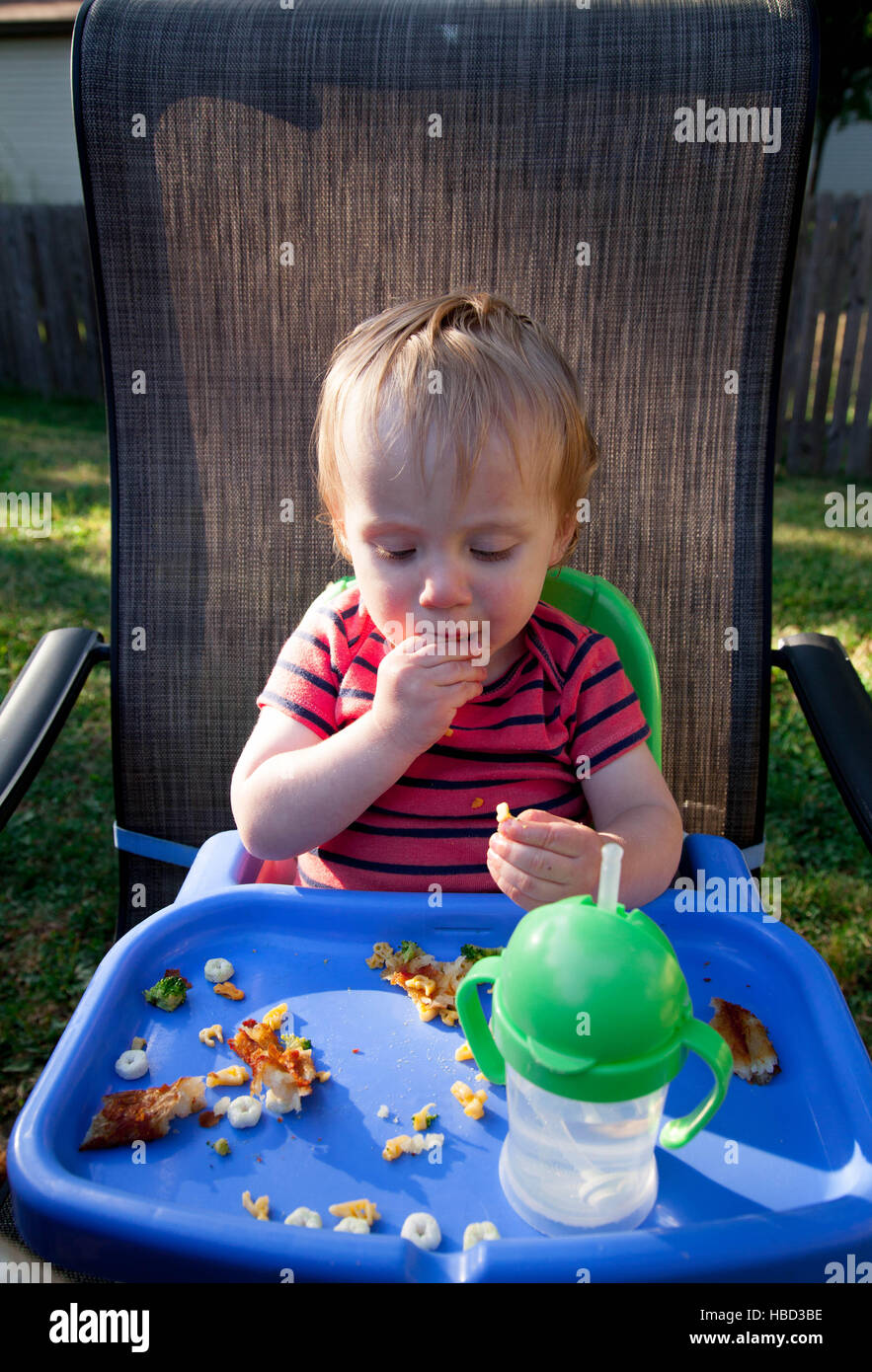 Caucasian baby boy sits in high chair and eats food at a picnic Stock Photo