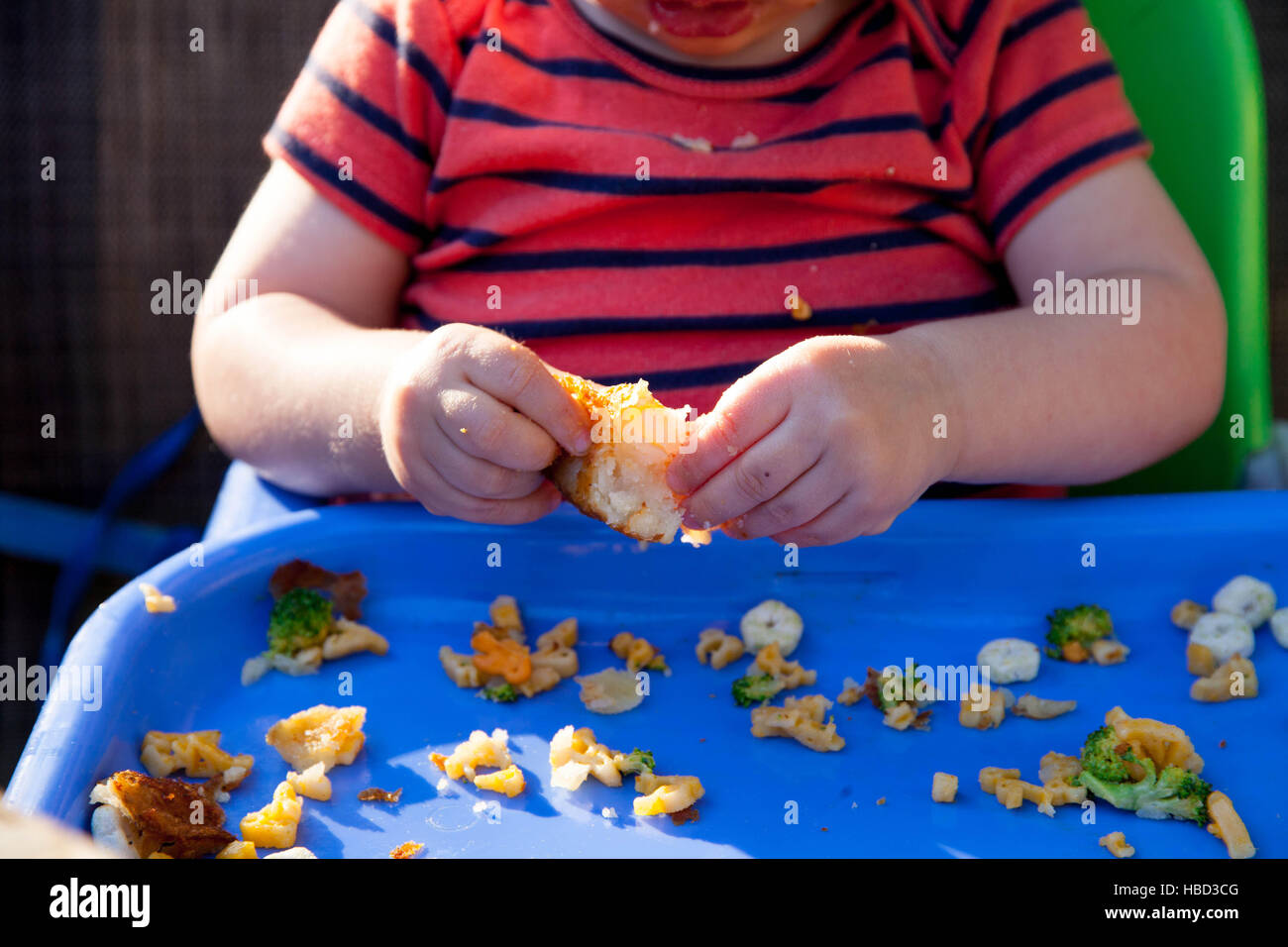Close up of A Caucasian baby boy sitting in a high chair and eating food at a picnic Stock Photo