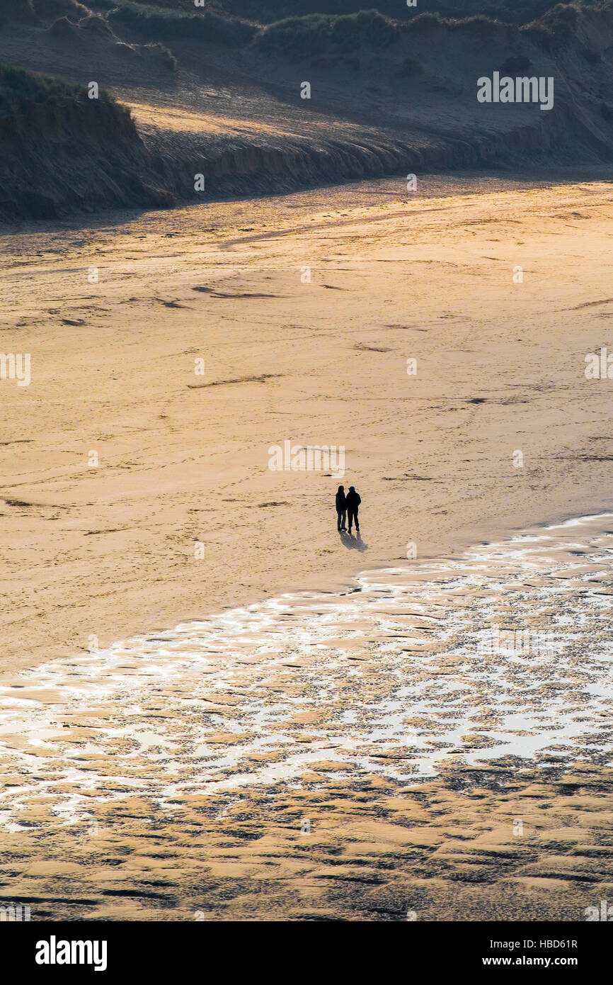 Two people seen in silhouette and from a distance on Crantock Beach in Newquay, Cornwall. Stock Photo