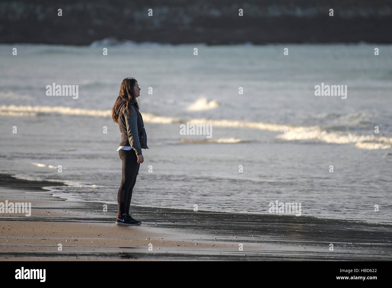 A woman gazes out to sea as she stands on Fistral Beach in Newquay, Cornwall. Stock Photo