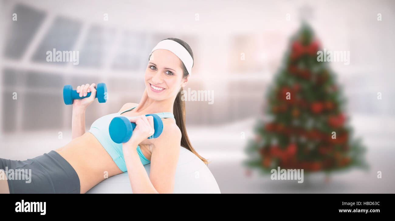 Composite image of smiling fit woman exercising with dumbbells on fitness ball Stock Photo