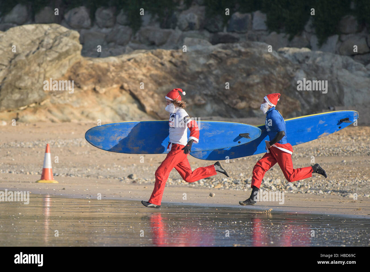 Surfing Santas race along the beach in the annual fund-raising Santa Surfing competition on a very chilly Fistral Beach in Newquay, Cornwall. UK. Stock Photo