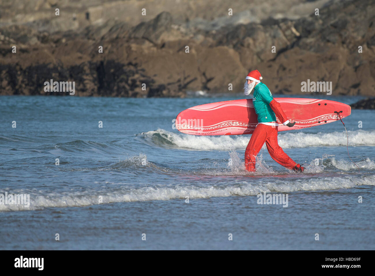 A surfing Santa running into the sea during the annual fund-raising Santa Surfing competition on a very chilly Fistral Beach in Newquay, Cornwall. Stock Photo