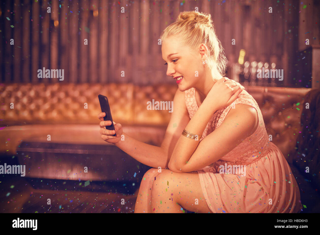 Composite image of beautiful woman sitting on sofa and using mobile phone Stock Photo