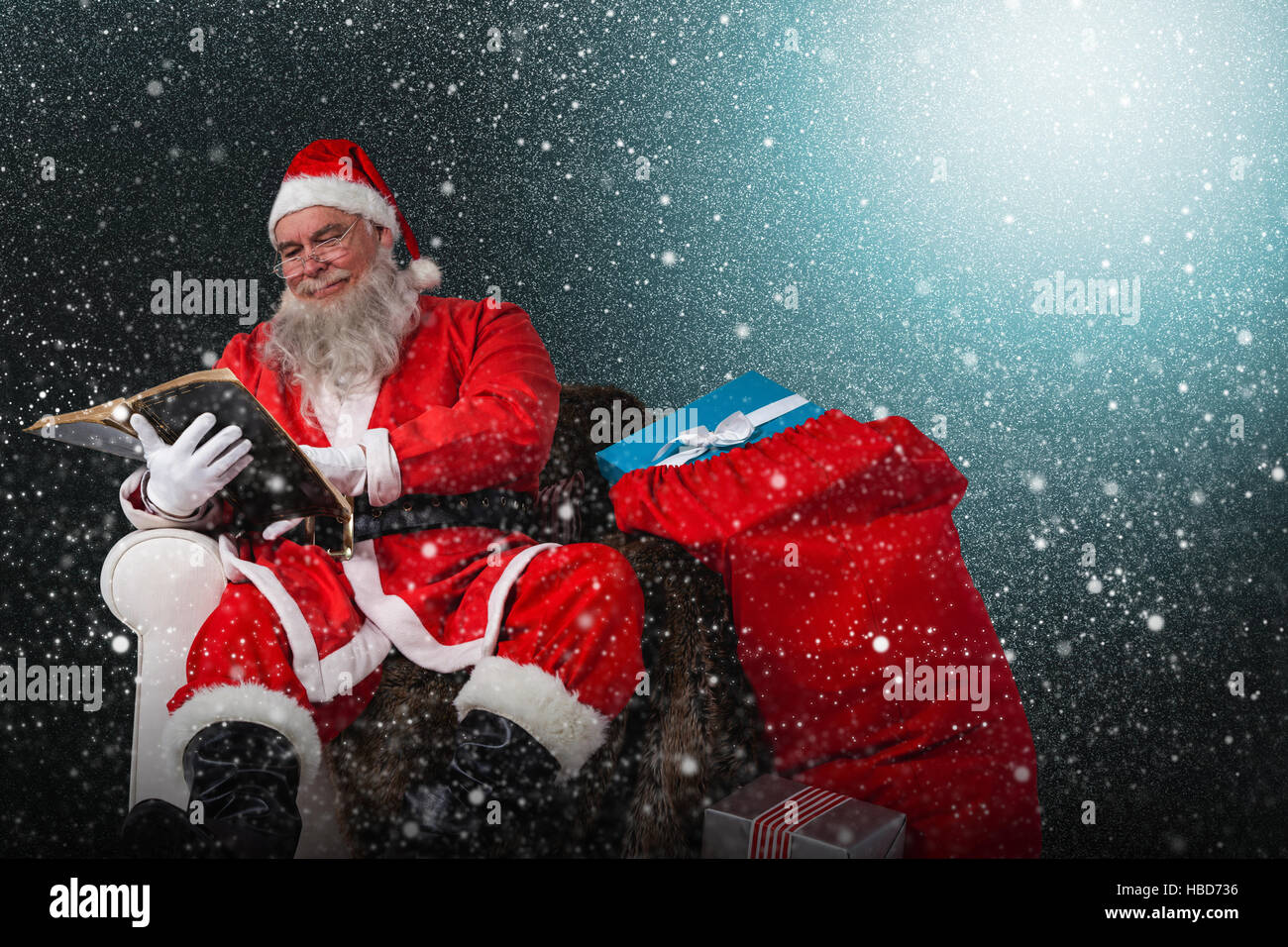 Composite image of santa reading bible with sack of christmas present beside him Stock Photo