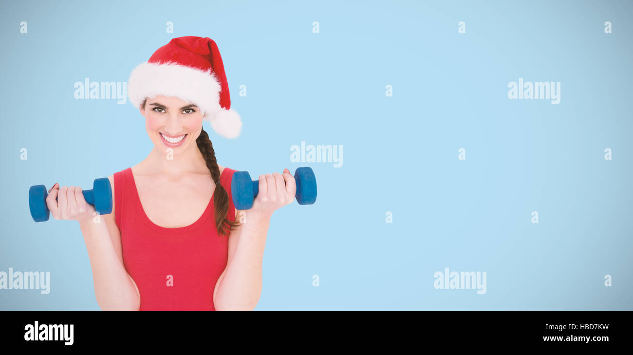 Composite image of festive fit brunette holding dumbbells Stock Photo