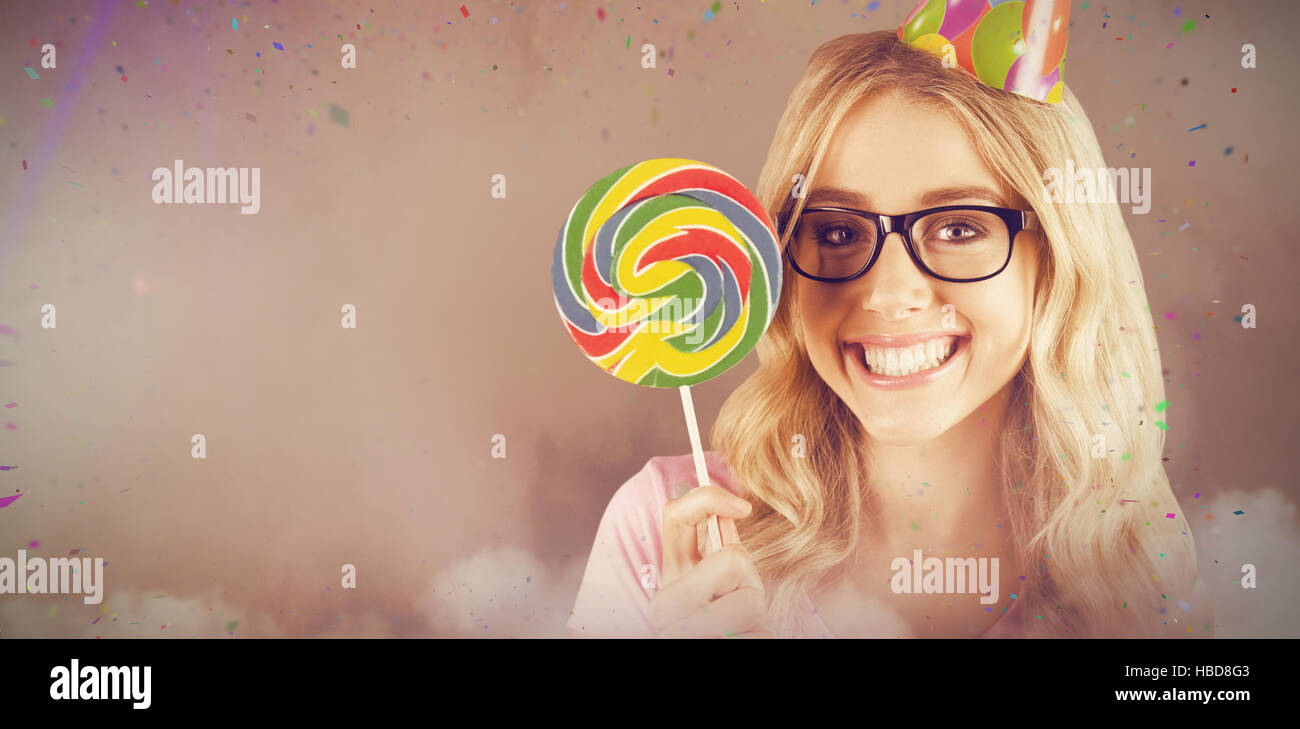 Composite image of portrait of a hipster with a party hat holding a lollipop Stock Photo