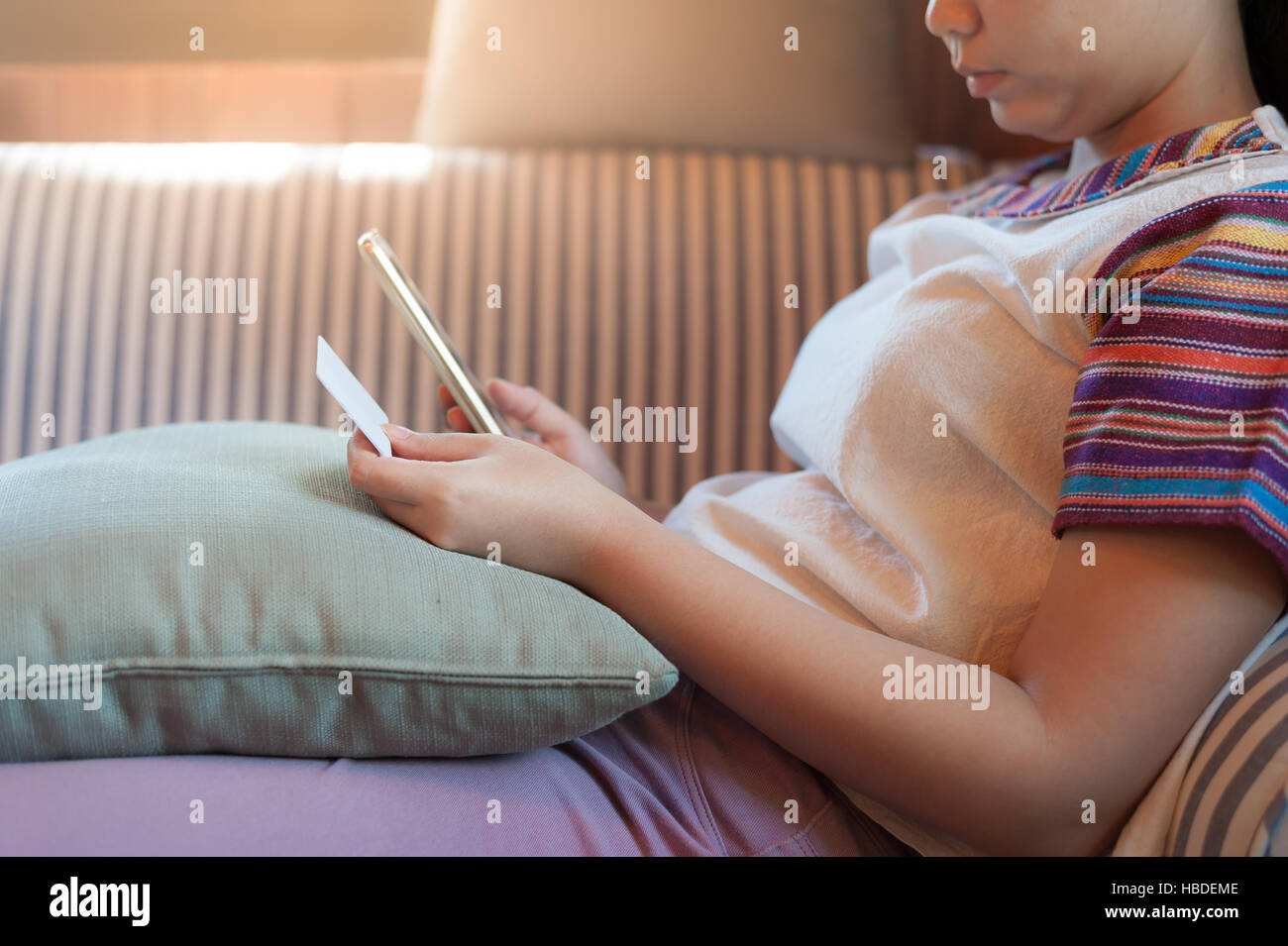 Trendy weekend lifestyle. Young woman using phone for on line shopping and another hand holding credit card while sitting on a couch. Shopping at home Stock Photo