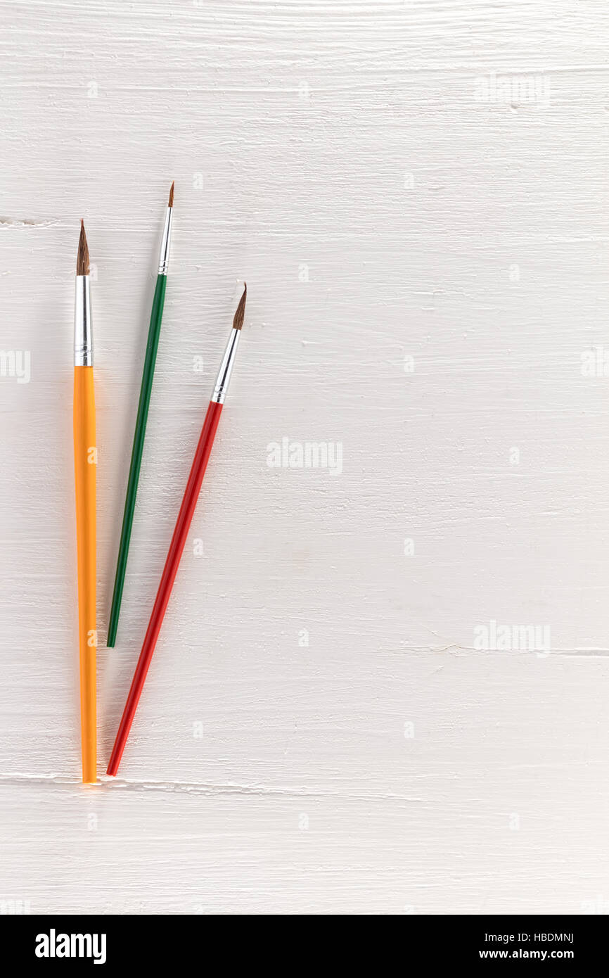 yellow, red and green paintbrush on a textured white table, free space for text Stock Photo