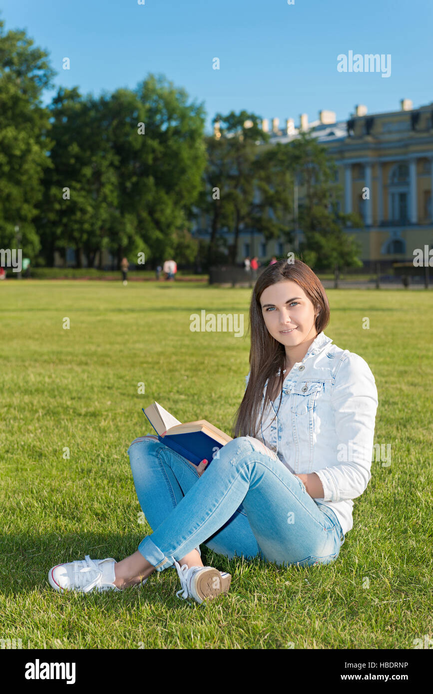 Girl-student sit on lawn and reads textbook Stock Photo - Alamy