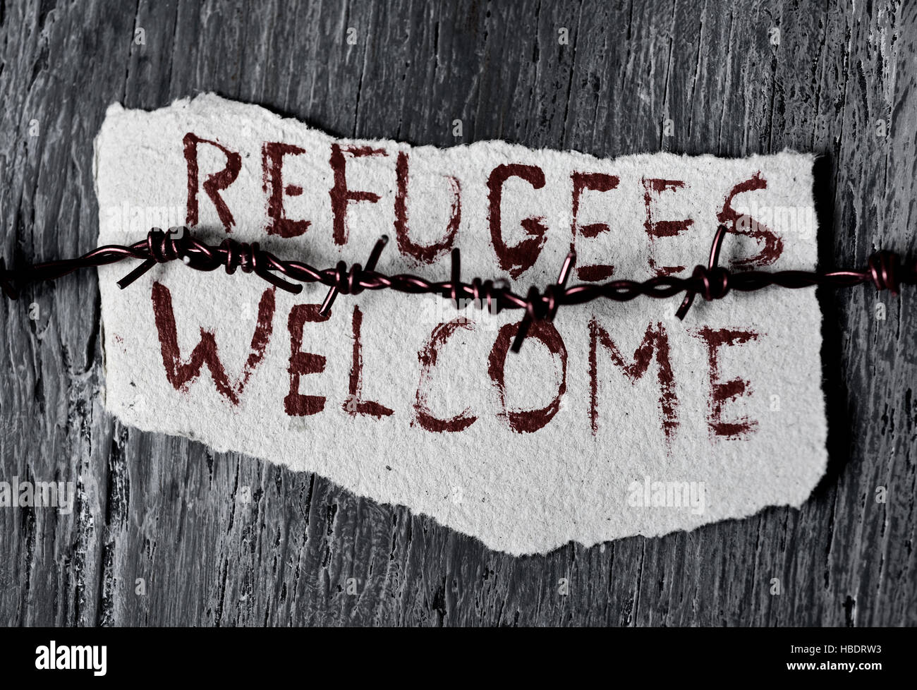 closeup of a barbed wire and a piece of paper with the text refugees welcome handwritten in it on a rustic wooden surface Stock Photo