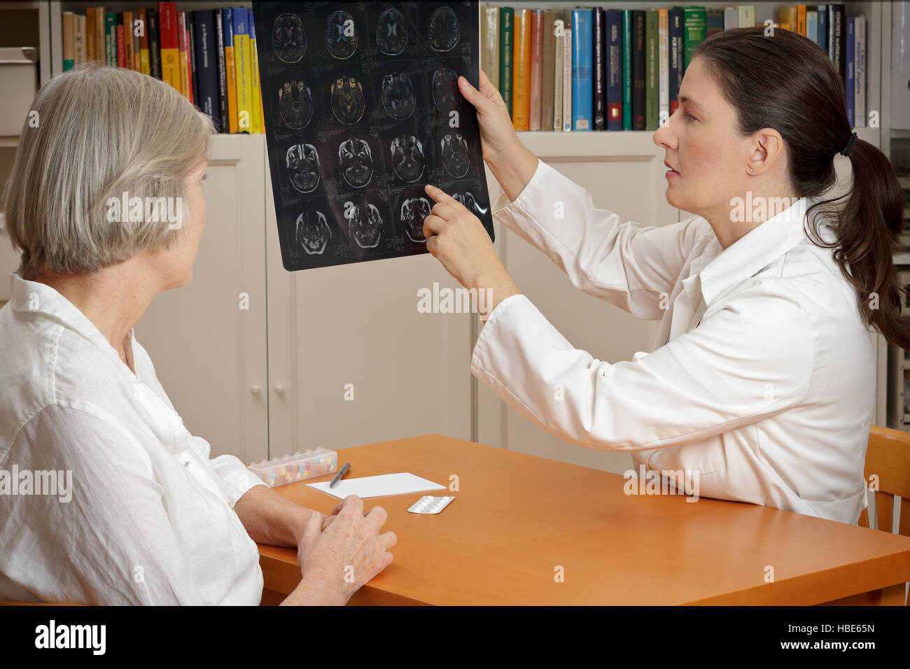 2 women in a  surgery: middle aged doctor in lab coat showing her senior patient magnetic resonance images of her head Stock Photo