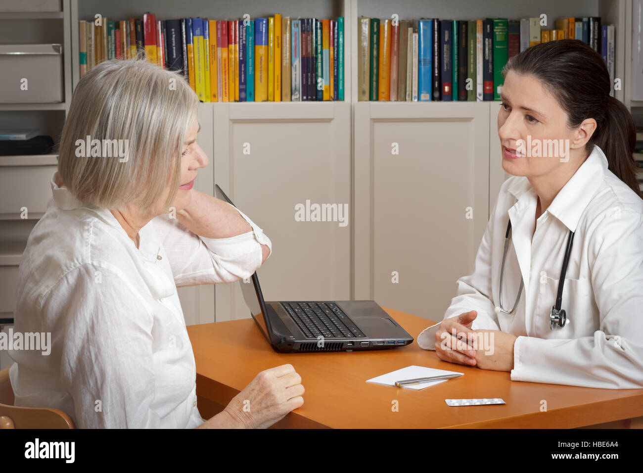 Old woman consulting an empathic female doctor considering acute neck pain caused by muscular tension Stock Photo