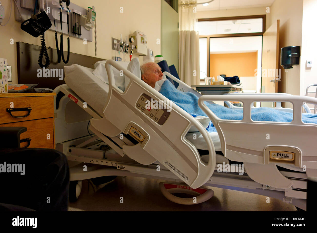 An elderly man lying in a bed in a hospital showing bed, room and equipment Stock Photo