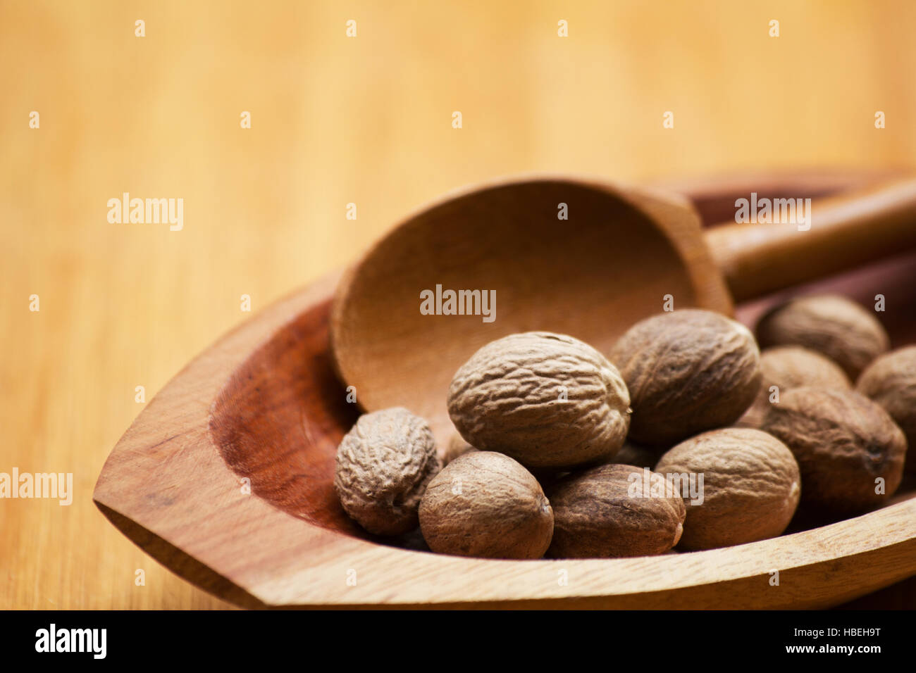 Nutmegs (Myristica fragrans) and wooden spoon in a bowl on a wooden table Stock Photo
