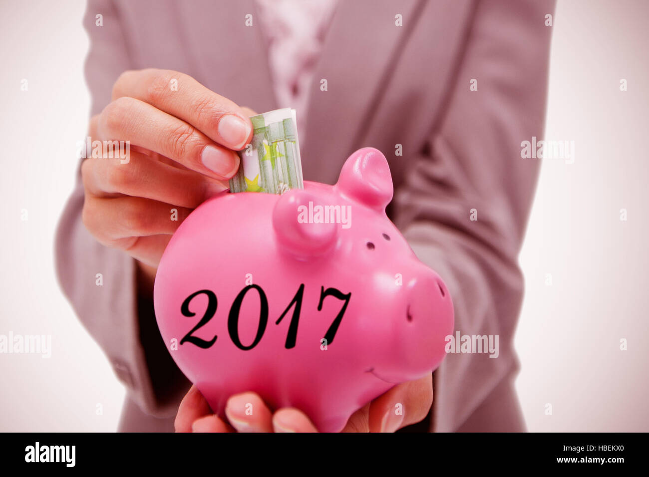 Composite image of money being put into piggy bank by smiling businesswoman Stock Photo