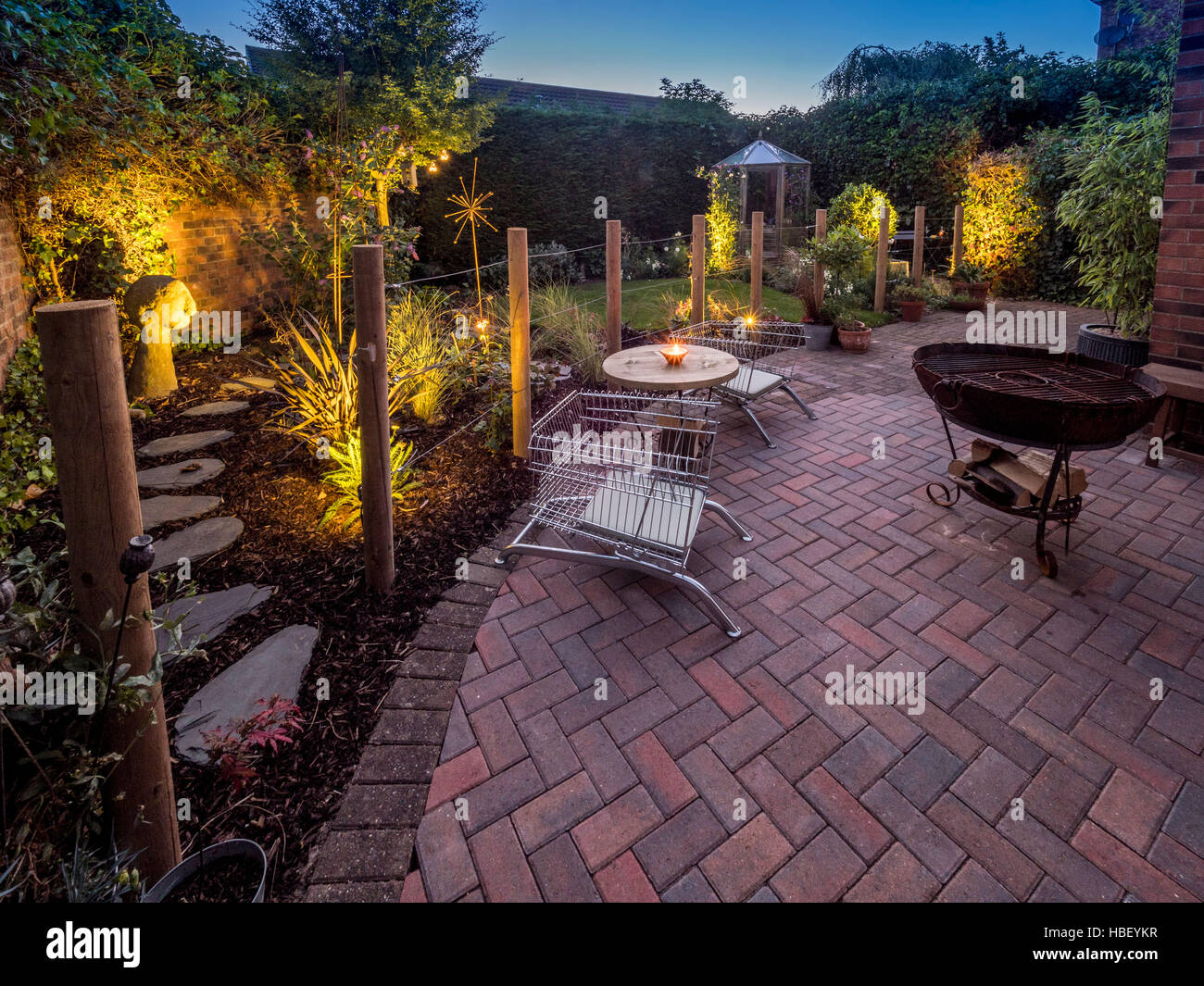 Modern garden design at dusk with contemporary wire upcycled shopping trolley chairs for seating and large Kadai firebowl Stock Photo