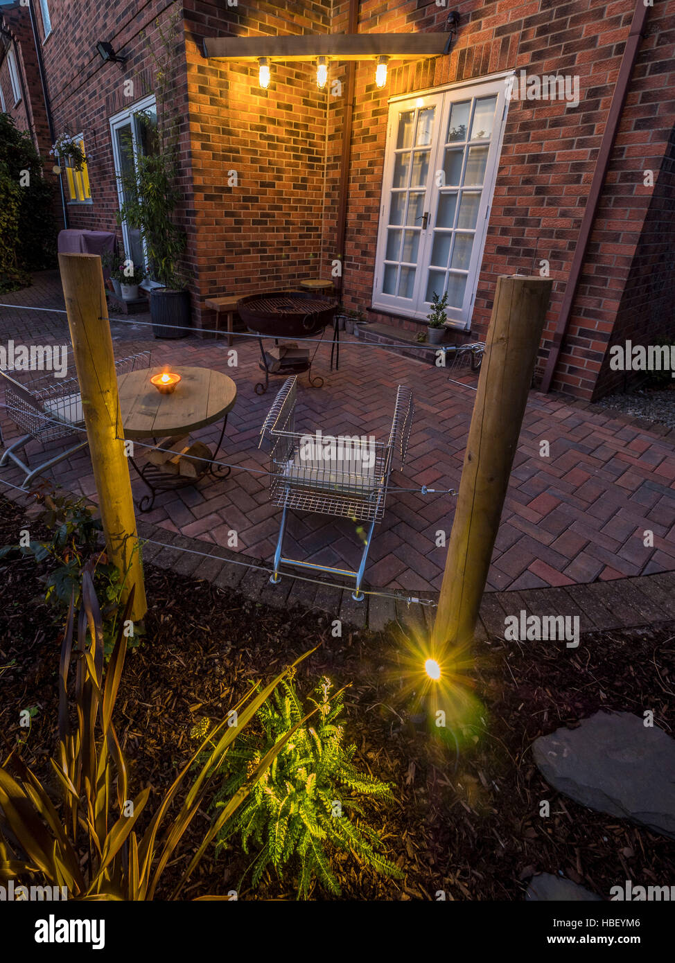 Modern garden design at dusk with contemporary upcycled shopping trolley chairs for seating and large Kadai firebowl. UK Stock Photo