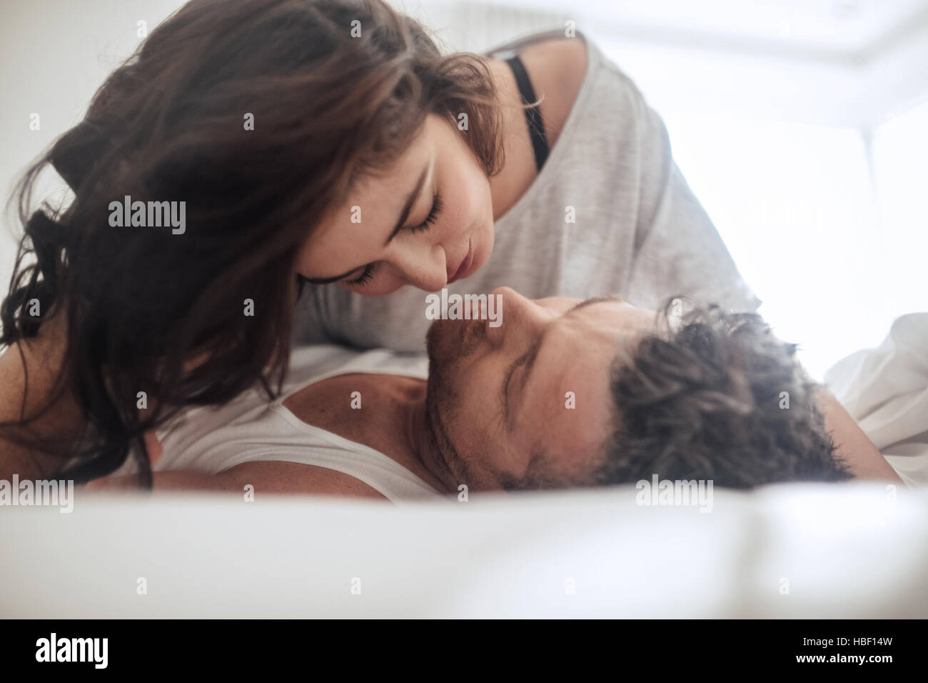 Young couple caressing lying in bed together. Couple in a relationship kissing and cuddling. Stock Photo