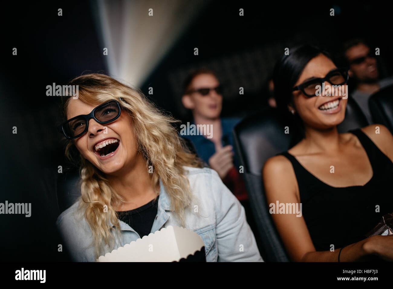Female friends watching 3d movie and laughing in cinema. Happy young women watching 3d film in theater. Stock Photo