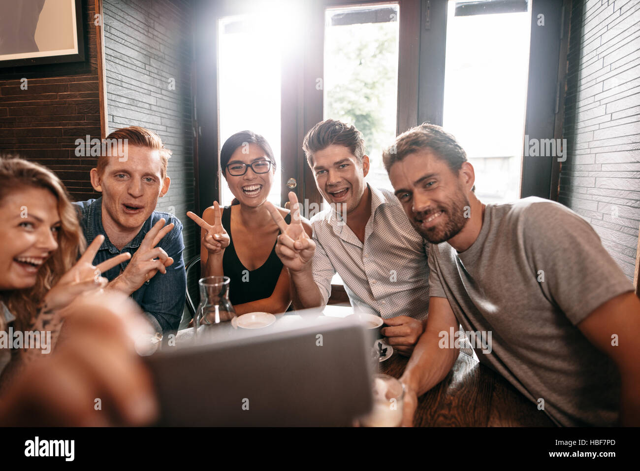 Multiracial people having fun at cafe taking a selfie with mobile phone. Group of young friends sitting  at restaurant taking self portrait with smart Stock Photo