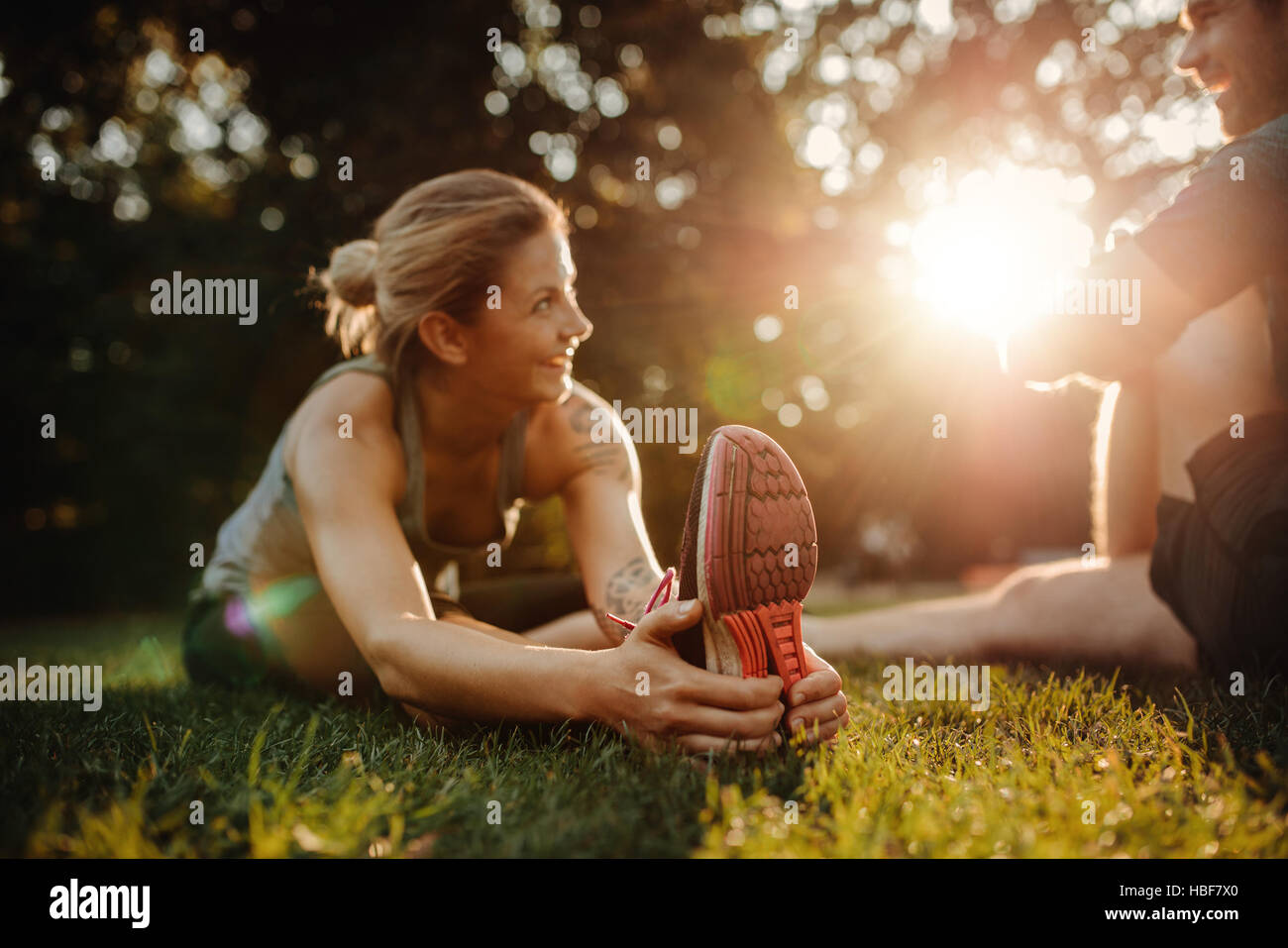 Beautiful young woman exercising at park. Caucasian couple doing morning workout in park, focus on feet and hands. Stock Photo