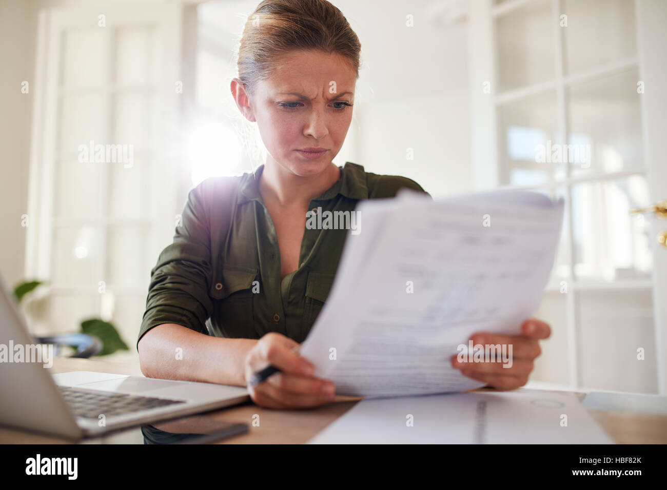Portrait of young female sitting at table reading documents. Woman busy working at home office. Stock Photo