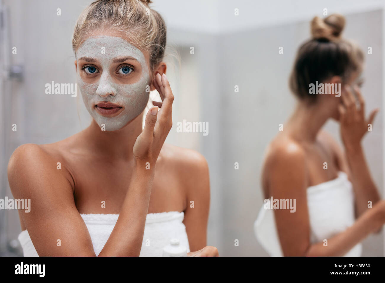 Close up shot of beautiful young woman doing beauty treatment on her face skin. Female applying facial mask in bathroom. Stock Photo