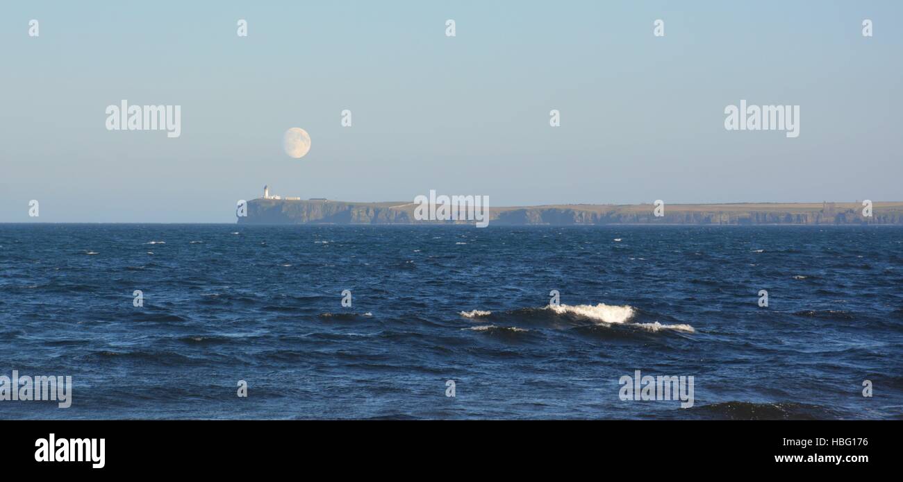 Moonrise above a lighthouse in Wick with sea in the foreground Stock Photo