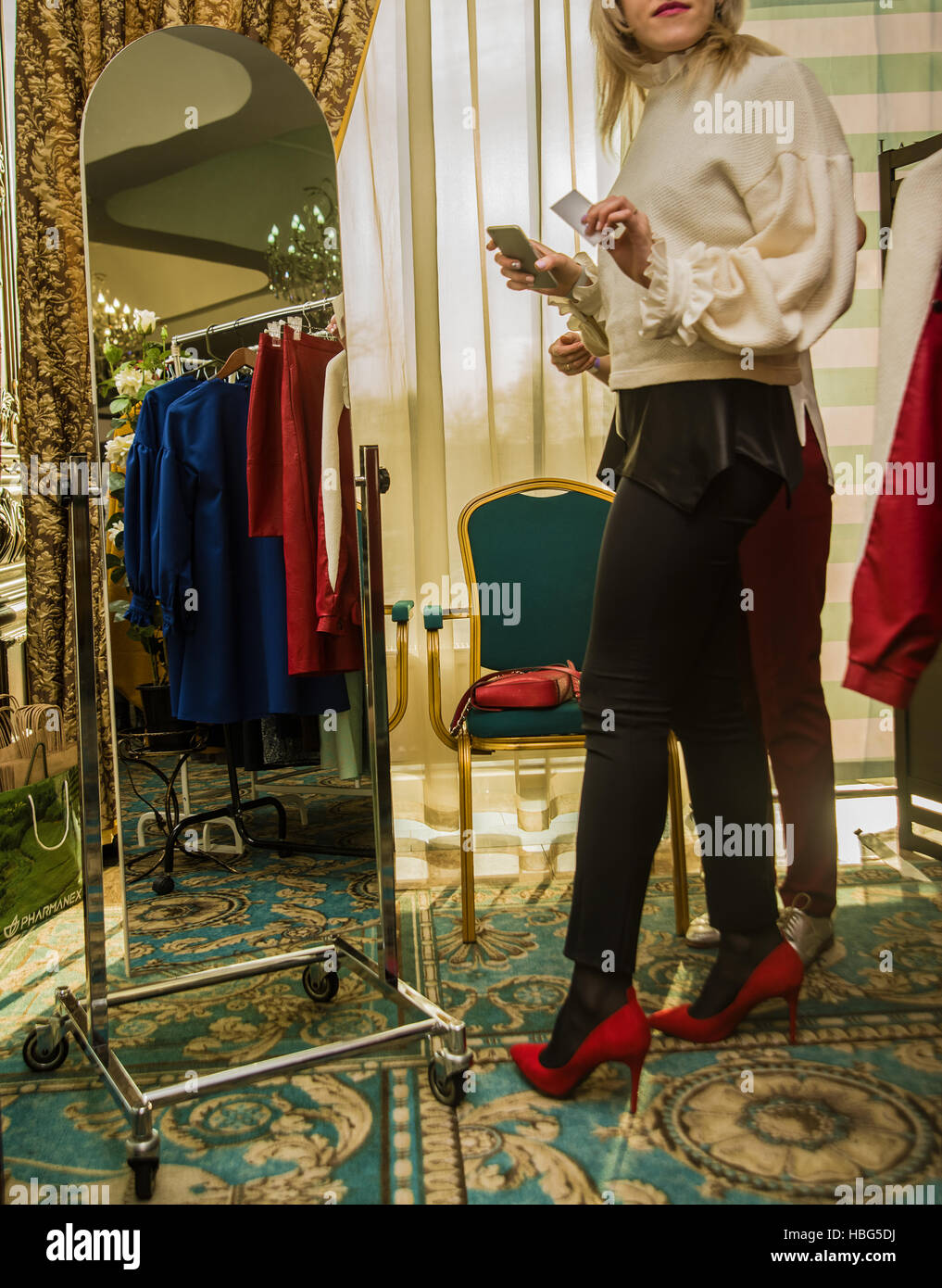 no face. unrecognizable person. young woman in a red high heel shoes looks in the mirror and choose clothes Stock Photo